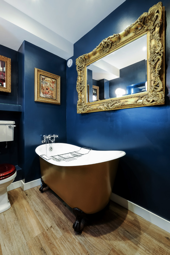 Imagen de cuarto de baño bohemio pequeño con armarios tipo mueble, puertas de armario de madera oscura, bañera con patas, sanitario de dos piezas, paredes azules, suelo de madera clara y lavabo con pedestal