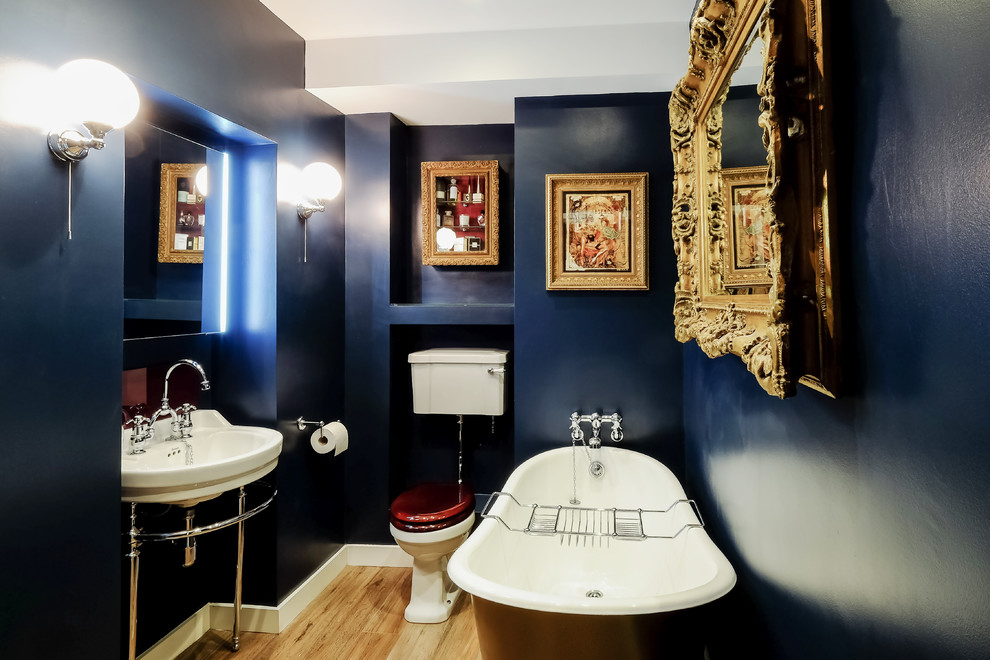 Diseño de cuarto de baño infantil clásico pequeño con armarios tipo mueble, puertas de armario de madera oscura, bañera con patas, sanitario de dos piezas, paredes azules, suelo de madera clara y lavabo tipo consola