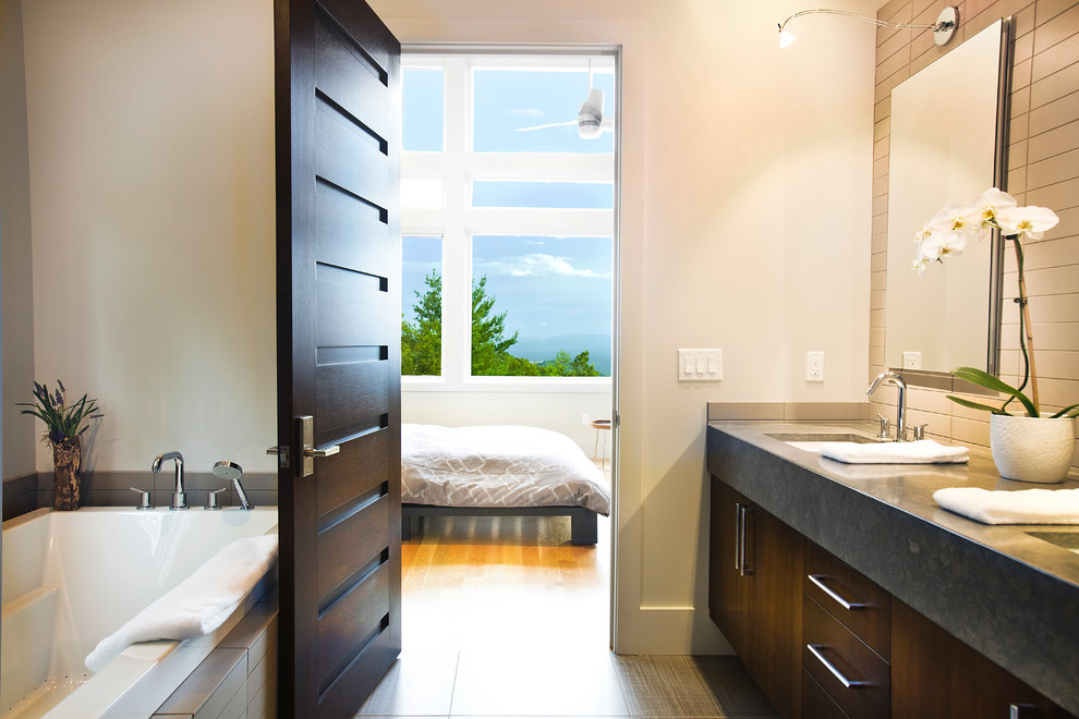 Modelo de cuarto de baño contemporáneo con lavabo bajoencimera, armarios con paneles lisos, puertas de armario de madera en tonos medios, bañera encastrada y baldosas y/o azulejos grises