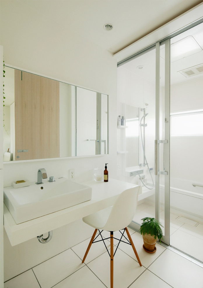 Cette image montre une salle de bain design avec un mur blanc, une vasque, une baignoire en alcôve, un espace douche bain, un carrelage blanc, un sol blanc et aucune cabine.