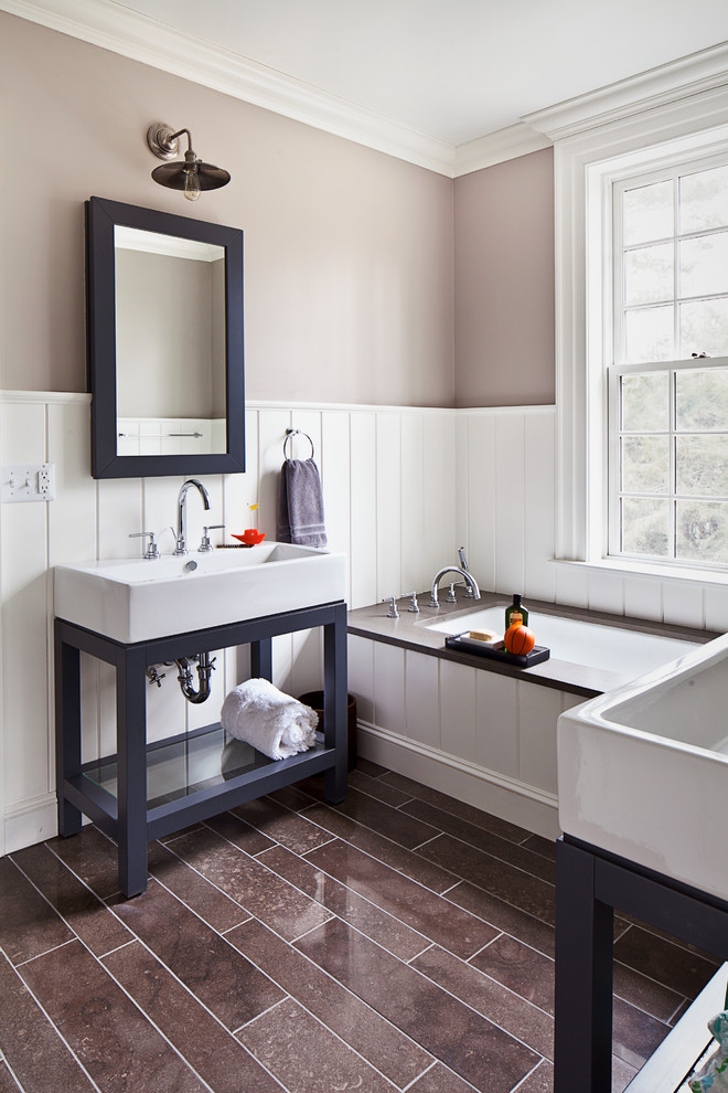 Inredning av ett klassiskt badrum, med beige väggar, ett fristående handfat, svarta skåp och ett undermonterat badkar