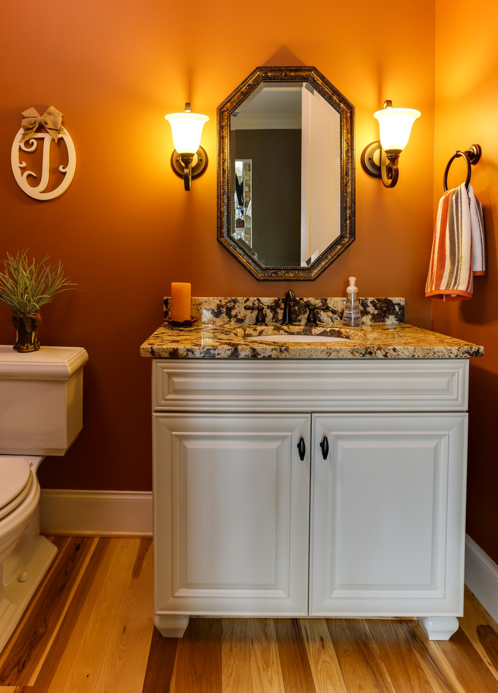 Example of a small classic 3/4 medium tone wood floor bathroom design in Raleigh with raised-panel cabinets, white cabinets, granite countertops and orange walls