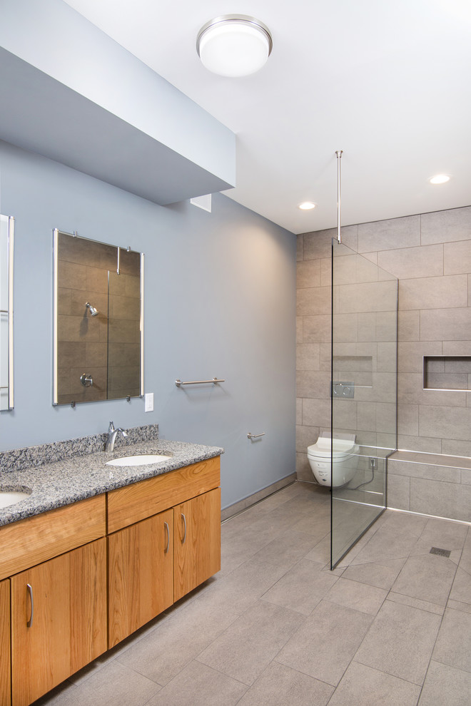 Example of a large trendy master gray tile and porcelain tile porcelain tile and beige floor bathroom design in Detroit with flat-panel cabinets, light wood cabinets, a wall-mount toilet, gray walls, an undermount sink, granite countertops and beige countertops