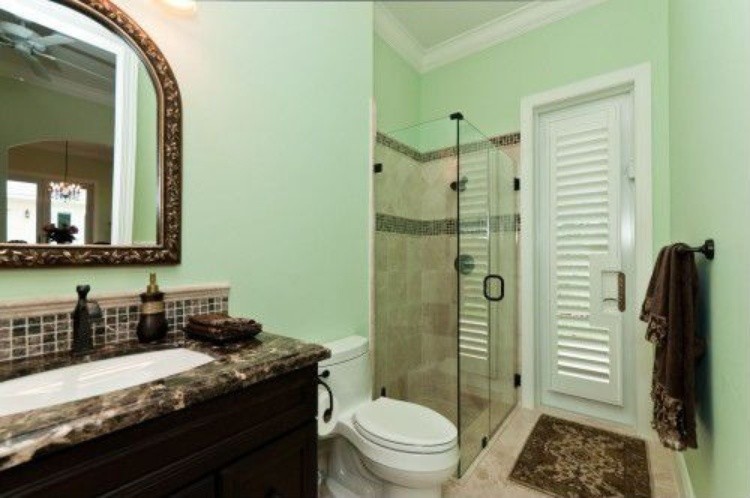 Mittelgroßes Klassisches Duschbad mit profilierten Schrankfronten, dunklen Holzschränken, Eckdusche, Toilette mit Aufsatzspülkasten, beigen Fliesen, Keramikfliesen, grüner Wandfarbe, Keramikboden, Unterbauwaschbecken und Granit-Waschbecken/Waschtisch in Miami