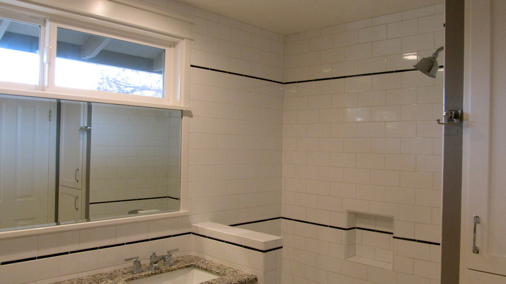 Amerikansk inredning av ett badrum, med ett undermonterad handfat, ett badkar i en alkov, en dusch/badkar-kombination, en toalettstol med separat cisternkåpa, skåp i shakerstil, vita skåp, granitbänkskiva, vit kakel och keramikplattor