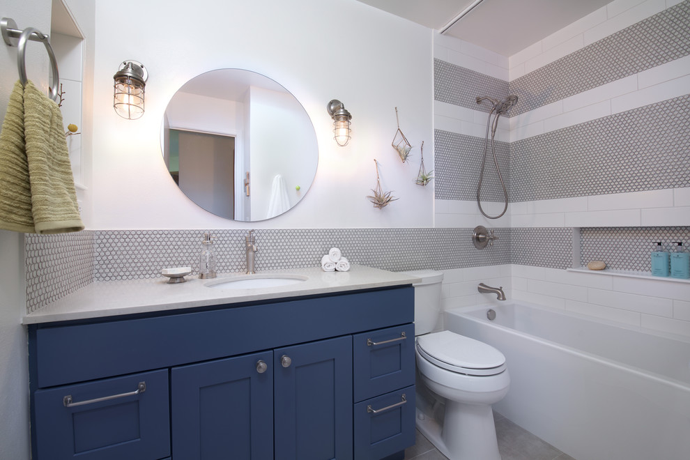 Idées déco pour une petite salle de bain industrielle pour enfant avec un placard à porte shaker, des portes de placard bleues, un bain bouillonnant, un carrelage blanc, des carreaux de porcelaine, un mur blanc, un sol en carrelage de porcelaine, un lavabo encastré, un plan de toilette en quartz modifié et un sol gris.