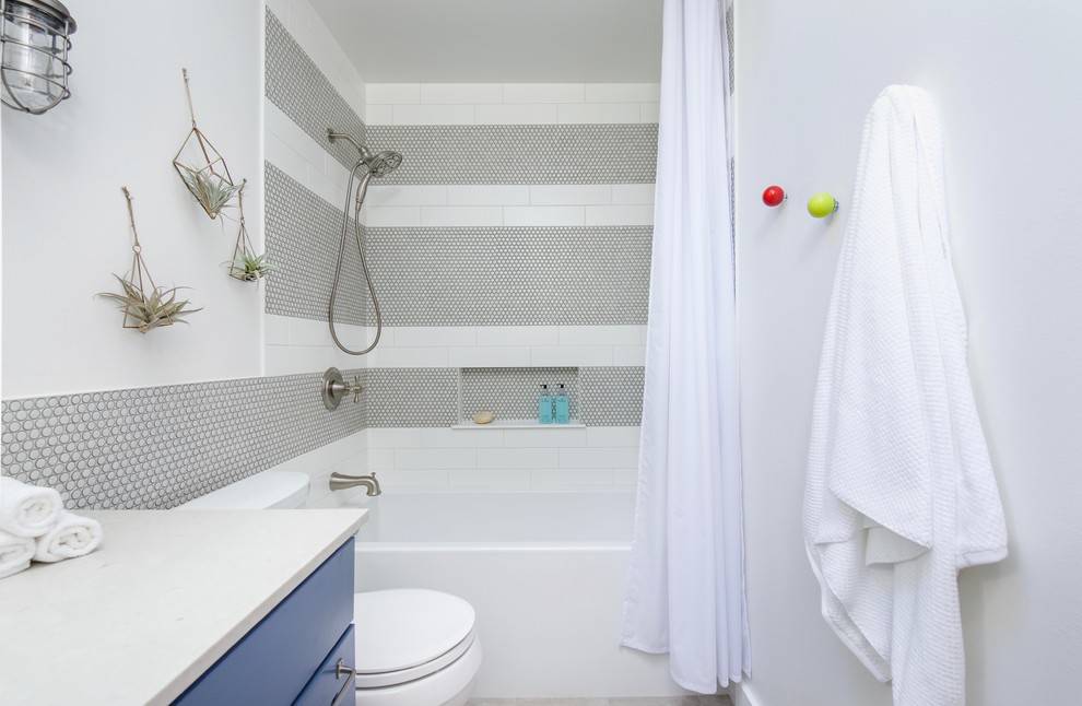 Exemple d'une petite salle de bain industrielle pour enfant avec un placard à porte shaker, des portes de placard bleues, un bain bouillonnant, un carrelage blanc, des carreaux de porcelaine, un mur blanc, un sol en carrelage de porcelaine, un lavabo encastré, un plan de toilette en quartz modifié et un sol gris.