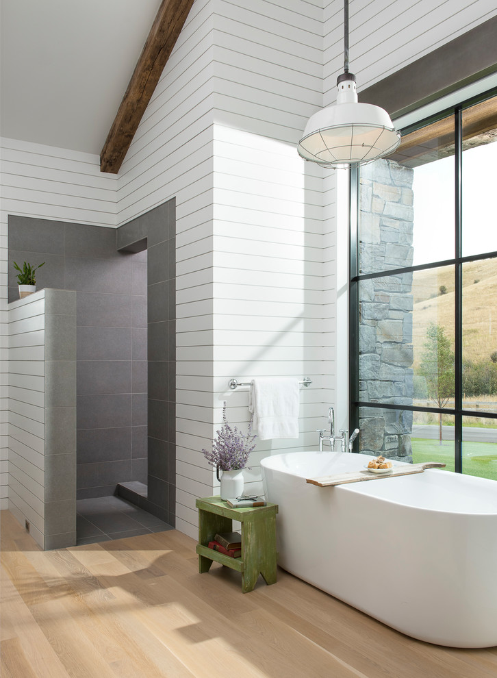 This is an example of an expansive farmhouse ensuite bathroom in Other with a freestanding bath, a walk-in shower, grey tiles, stone tiles, white walls, light hardwood flooring and an open shower.
