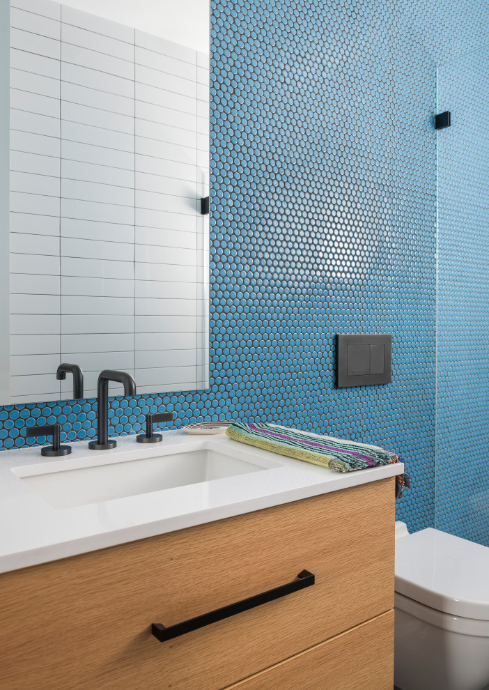 Modern inredning av ett vit vitt badrum för barn, med en vägghängd toalettstol, blå väggar, släta luckor, skåp i ljust trä, en dusch i en alkov, blå kakel, bänkskiva i kvarts, mosaik och ett undermonterad handfat