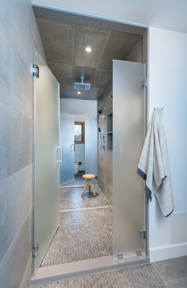 Modern inredning av ett en-suite badrum, med en dubbeldusch, dusch med gångjärnsdörr, en toalettstol med hel cisternkåpa, keramikplattor, vita väggar, klinkergolv i keramik och grått golv