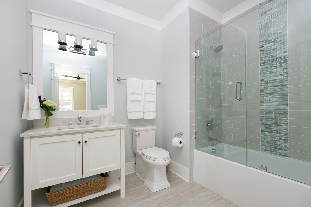 Klassisches Badezimmer mit weißen Schränken, Badewanne in Nische, Duschbadewanne, grauen Fliesen, grauer Wandfarbe, Unterbauwaschbecken, beigem Boden, Falttür-Duschabtrennung und weißer Waschtischplatte in Charleston