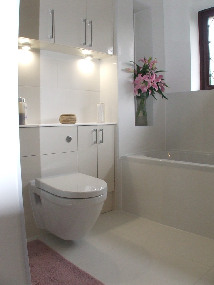 Modern inredning av ett mellanstort en-suite badrum, med ett väggmonterat handfat, släta luckor, beige skåp, bänkskiva i akrylsten, en dusch i en alkov, en vägghängd toalettstol, vit kakel, porslinskakel och vita väggar