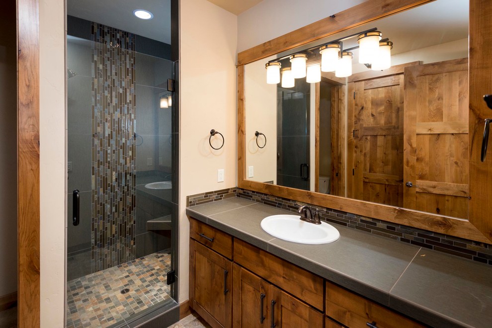Immagine di una stanza da bagno con doccia rustica con ante con riquadro incassato, ante in legno scuro, top piastrellato, pavimento con piastrelle in ceramica e lavabo da incasso