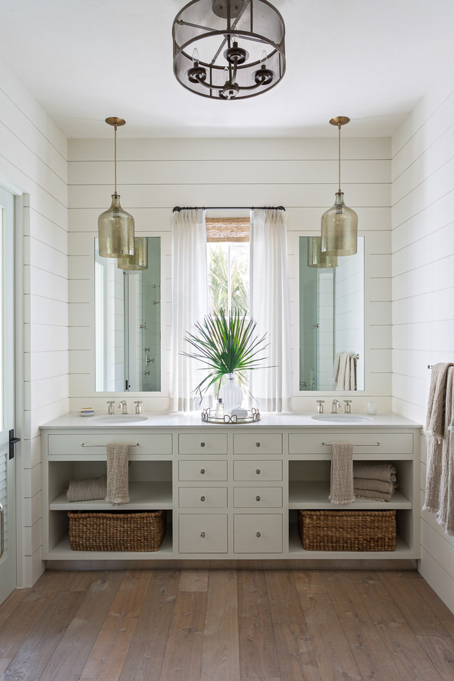 Maritimes Badezimmer En Suite mit offenen Schränken, grauen Schränken, weißer Wandfarbe, hellem Holzboden, Unterbauwaschbecken, weißer Waschtischplatte und Doppelwaschbecken in Charleston