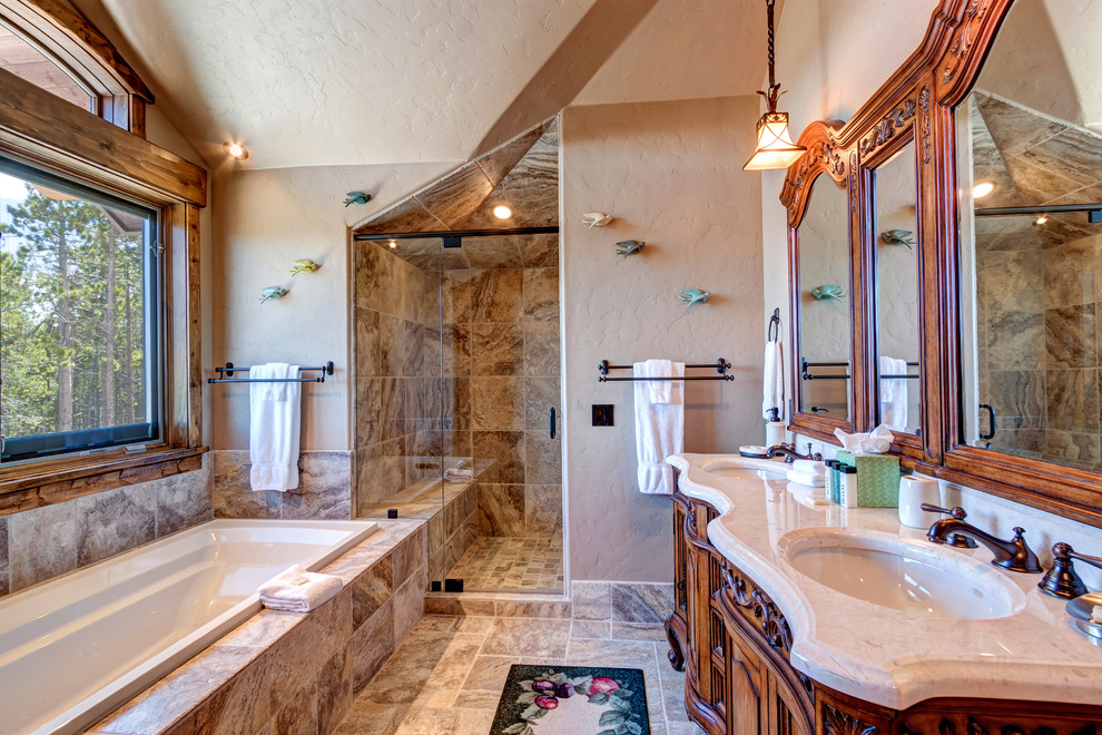 This is an example of a large rustic ensuite bathroom in Denver with an alcove shower, beige tiles, a hinged door, dark wood cabinets, a built-in bath, limestone tiles, red walls, limestone flooring, a submerged sink, limestone worktops, multi-coloured floors, multi-coloured worktops and recessed-panel cabinets.