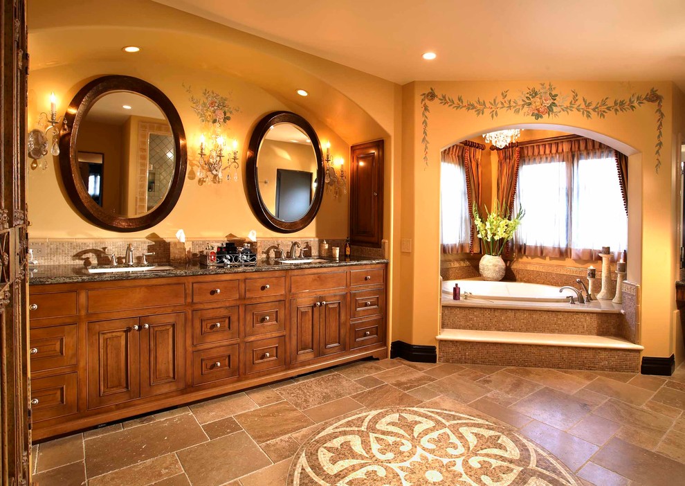 Cette photo montre une très grande salle de bain principale méditerranéenne en bois brun avec un placard avec porte à panneau surélevé, un plan de toilette en granite, une baignoire d'angle, un carrelage marron, mosaïque, un mur jaune, un sol en travertin et un lavabo posé.