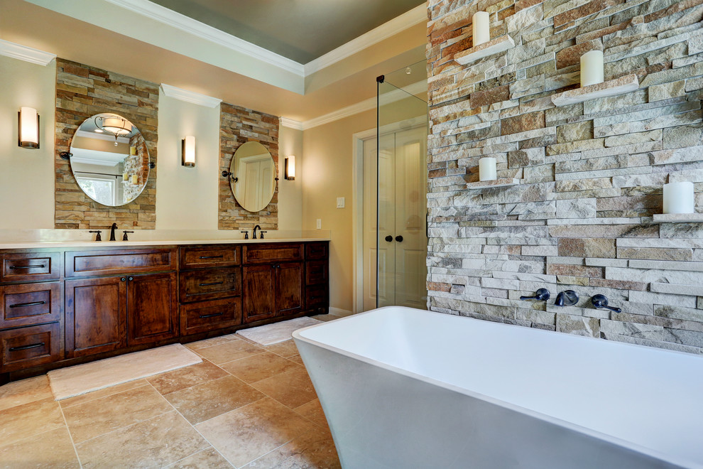 Photo of a large traditional ensuite bathroom in Houston with a built-in sink, recessed-panel cabinets, dark wood cabinets, marble worktops, a freestanding bath, a walk-in shower, beige tiles, stone tiles, beige walls and travertine flooring.