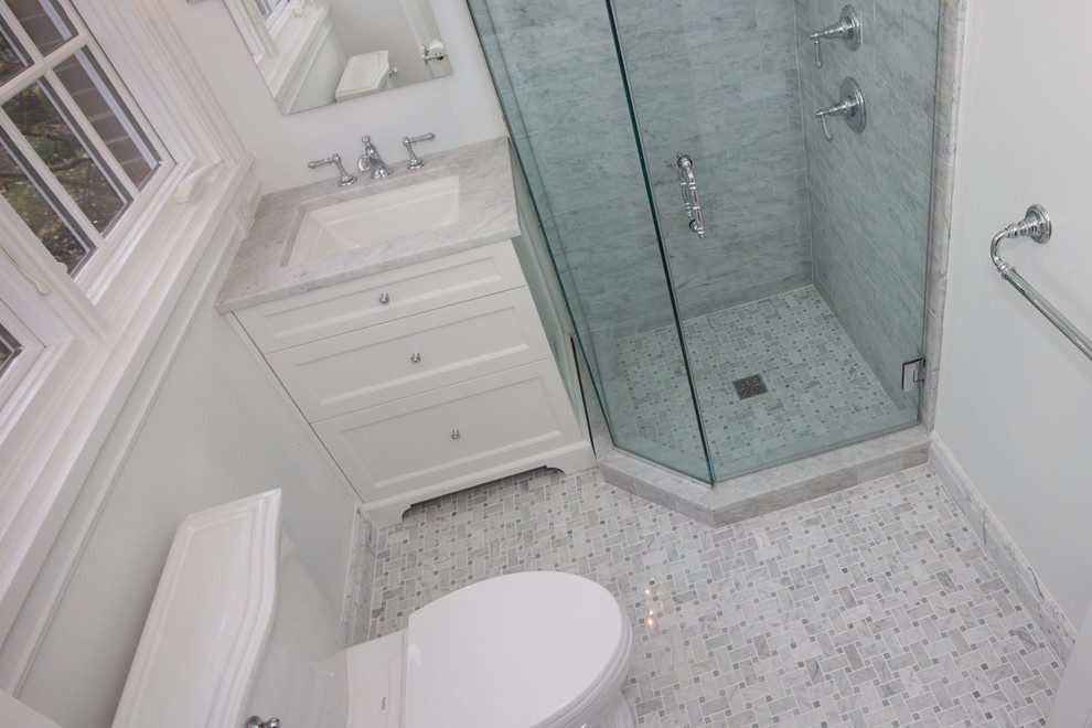 Foto på ett mellanstort funkis badrum med dusch, med luckor med profilerade fronter, vita skåp, en hörndusch, en toalettstol med hel cisternkåpa, grå kakel, vit kakel, stenkakel, vita väggar, marmorgolv, ett nedsänkt handfat och marmorbänkskiva