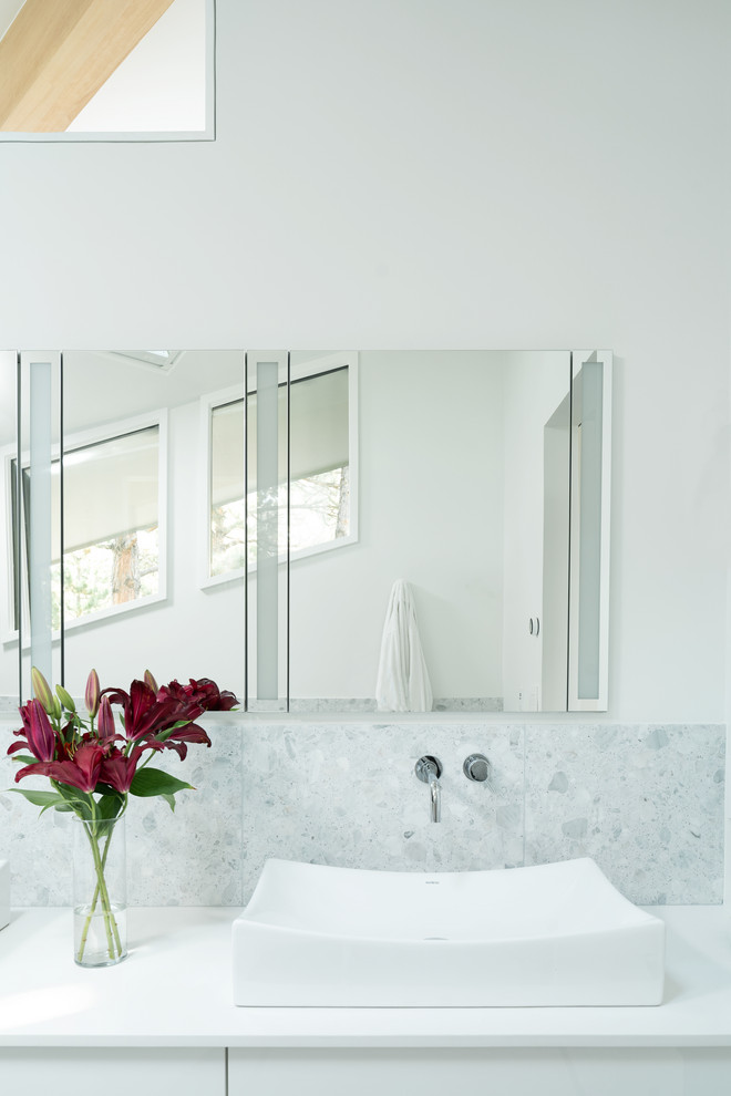 Стильный дизайн: главная ванная комната в стиле модернизм с плоскими фасадами, белыми фасадами, отдельно стоящей ванной, душем без бортиков, унитазом-моноблоком, белой плиткой, мраморной плиткой, белыми стенами, полом из терраццо, настольной раковиной, столешницей из искусственного кварца, белым полом, душем с раздвижными дверями и белой столешницей - последний тренд