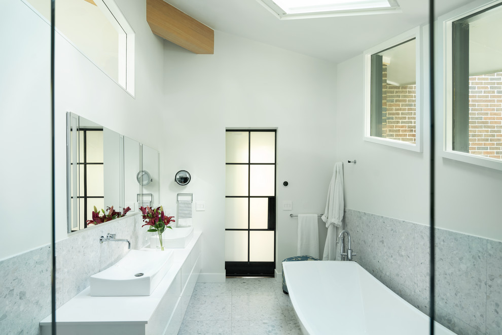 На фото: главная ванная комната в стиле модернизм с плоскими фасадами, белыми фасадами, отдельно стоящей ванной, душем без бортиков, унитазом-моноблоком, белой плиткой, мраморной плиткой, белыми стенами, полом из терраццо, настольной раковиной, столешницей из искусственного кварца, белым полом, душем с раздвижными дверями и белой столешницей с