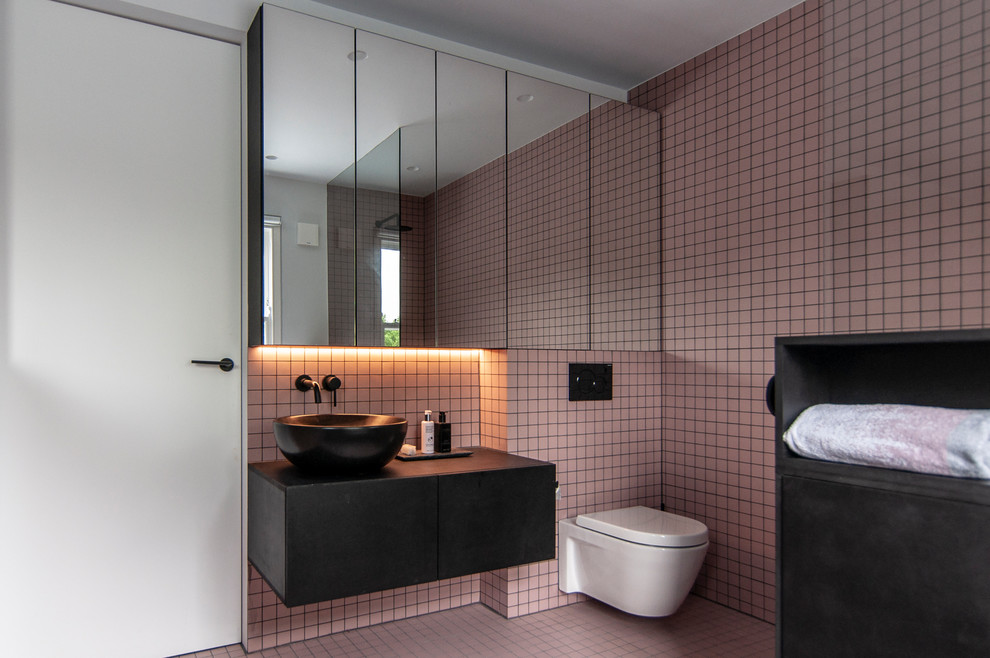 Idée de décoration pour une salle de bain design de taille moyenne avec un placard à porte plane, des portes de placard noires, WC suspendus, un carrelage rose, un mur rose, un sol rose, un plan de toilette noir et une vasque.