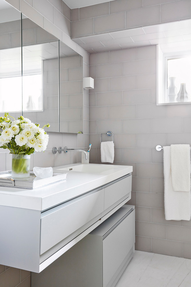 Cette image montre une salle de bain design avec un placard à porte plane, des portes de placard grises, un carrelage beige, un carrelage gris, un lavabo intégré, un sol blanc et un plan de toilette blanc.