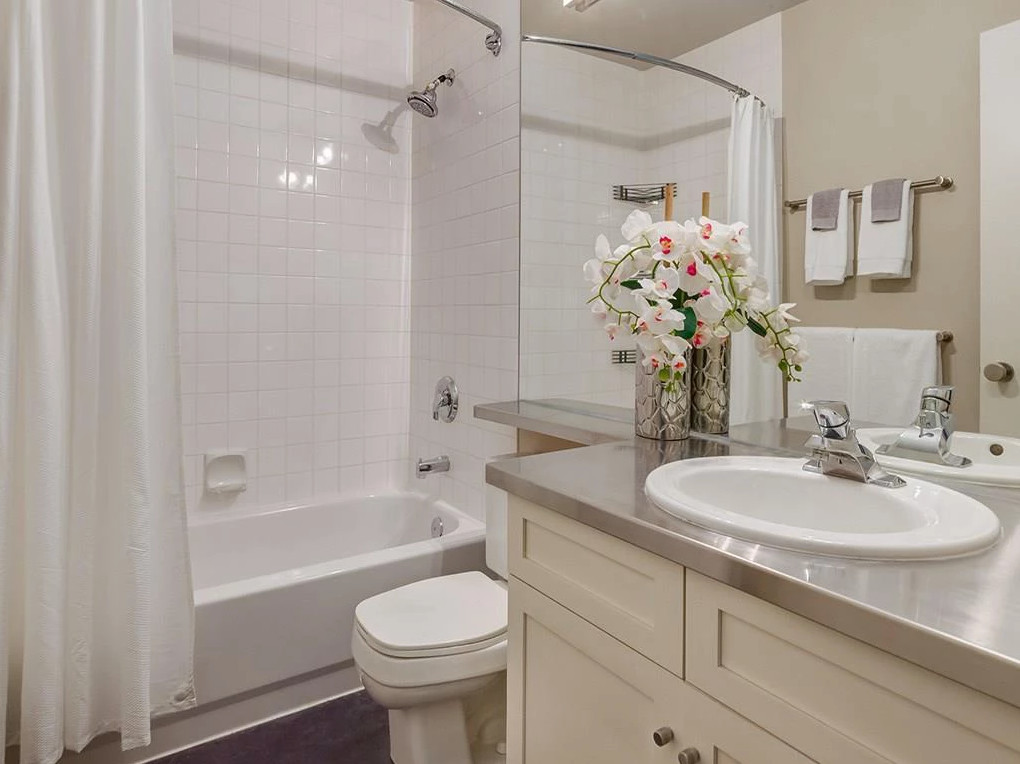 This is an example of a medium sized traditional shower room bathroom in Calgary with shaker cabinets, white cabinets, a shower/bath combination, a two-piece toilet, white tiles, ceramic tiles, beige walls, dark hardwood flooring, a built-in sink, zinc worktops, brown floors and a shower curtain.