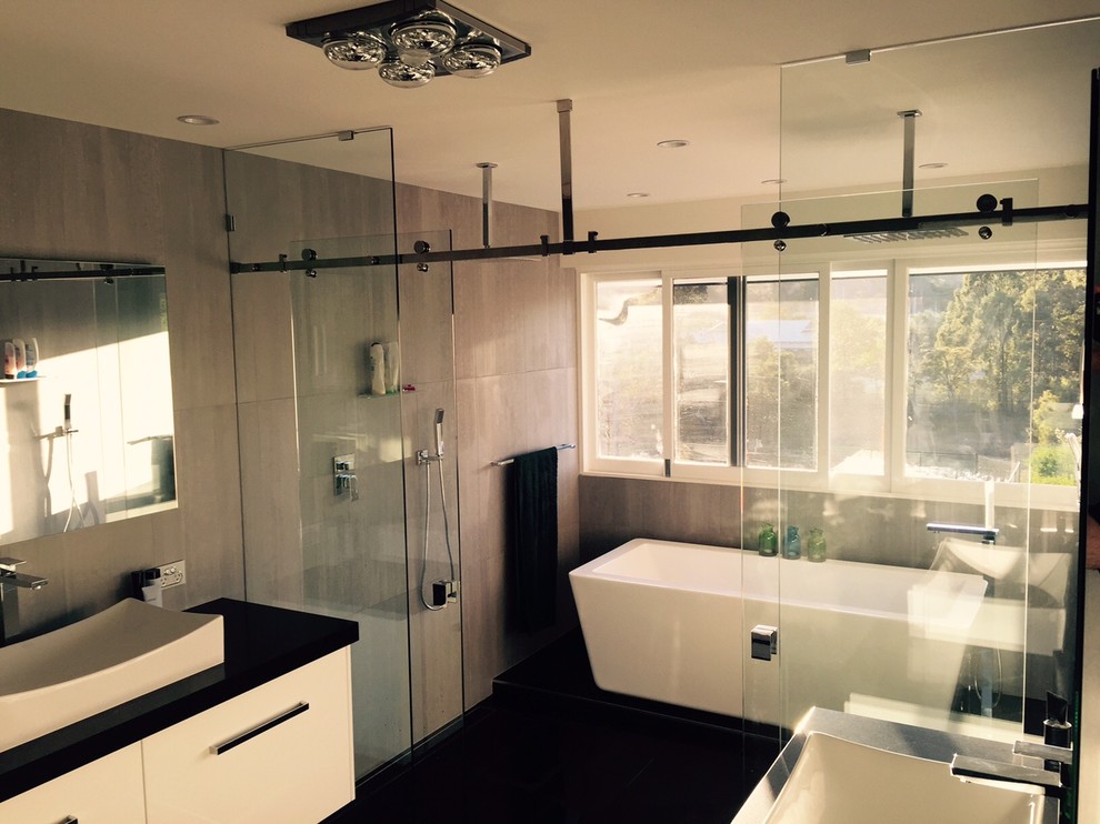 Design ideas for a large modern ensuite bathroom in Brisbane with a vessel sink, freestanding cabinets, engineered stone worktops, a freestanding bath, a double shower, a wall mounted toilet, grey tiles, porcelain tiles and porcelain flooring.