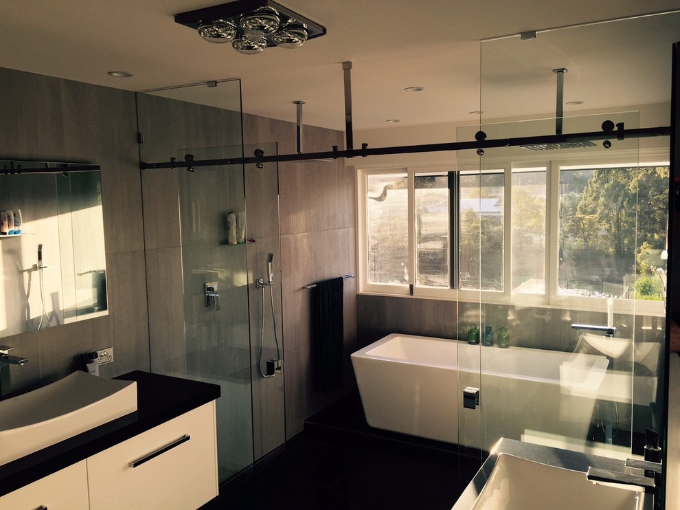 Design ideas for a large modern ensuite bathroom in Brisbane with a vessel sink, freestanding cabinets, engineered stone worktops, a freestanding bath, a double shower, a wall mounted toilet, grey tiles, porcelain tiles and porcelain flooring.