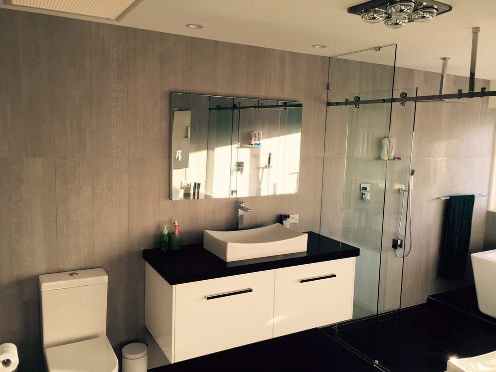 This is an example of a large modern ensuite bathroom in Brisbane with a vessel sink, freestanding cabinets, engineered stone worktops, a freestanding bath, a double shower, a wall mounted toilet, grey tiles, porcelain tiles and porcelain flooring.