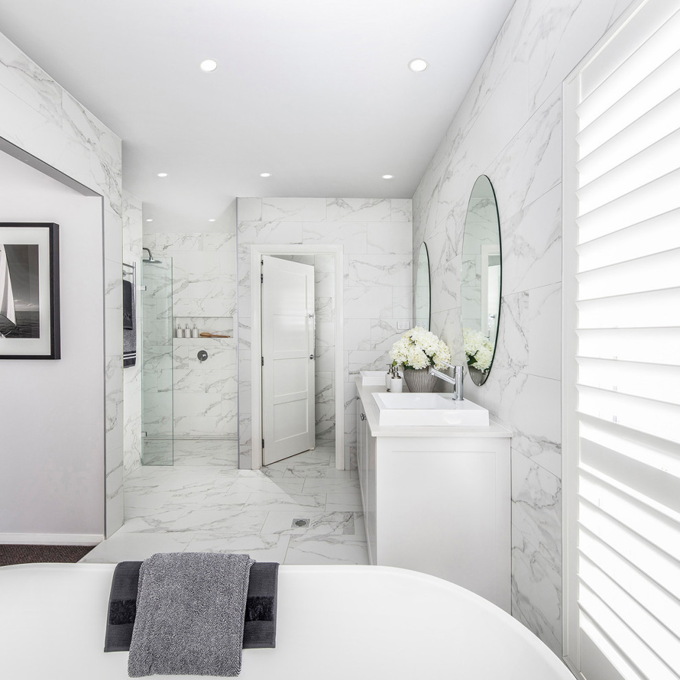 Стильный дизайн: большая главная ванная комната в классическом стиле с фасадами в стиле шейкер, белыми фасадами, полновстраиваемой ванной, угловым душем, белой плиткой, мраморной плиткой, белыми стенами, мраморным полом, накладной раковиной, столешницей из искусственного кварца, белым полом, душем с раздвижными дверями и белой столешницей - последний тренд