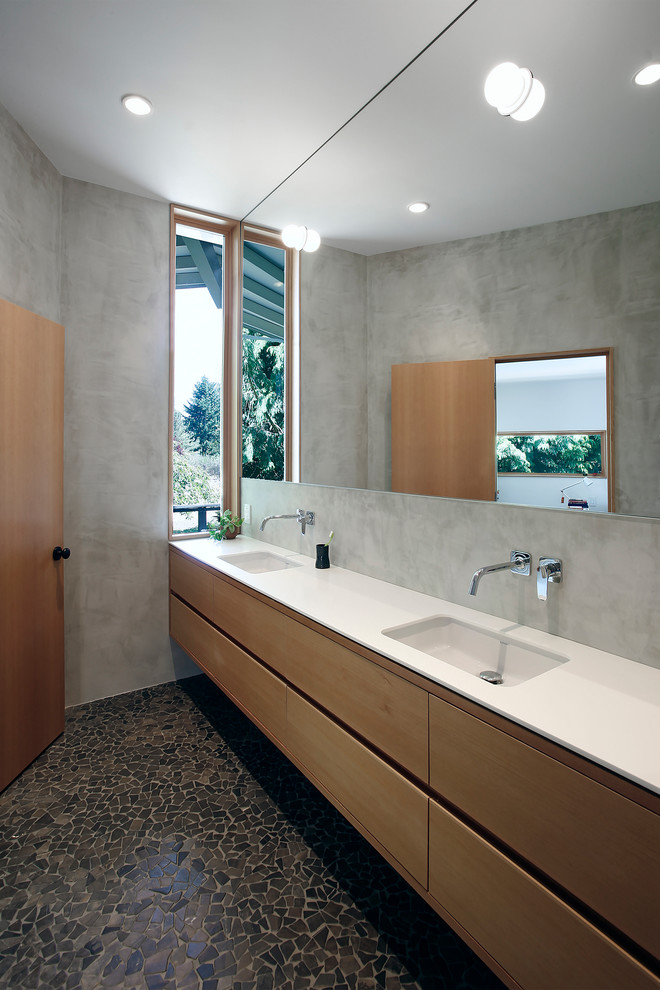 Cette image montre une grande salle de bain principale vintage en bois clair avec un placard à porte plane, un mur gris, un sol en galet, un lavabo encastré et un plan de toilette en quartz.