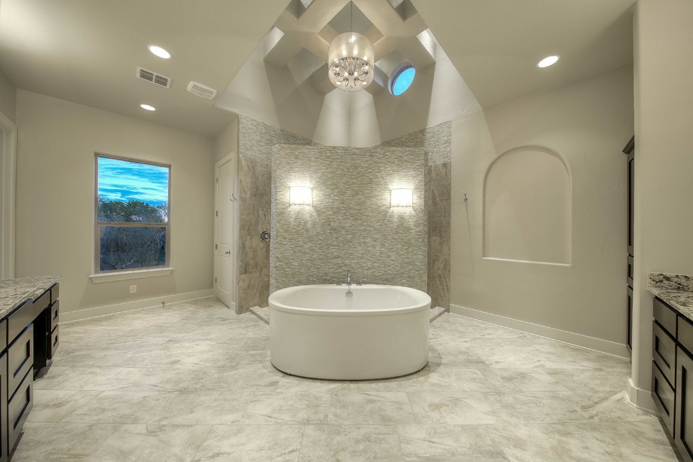 Modelo de cuarto de baño principal tradicional renovado grande con puertas de armario de madera en tonos medios, bañera exenta, ducha esquinera, baldosas y/o azulejos grises, paredes beige y encimera de granito