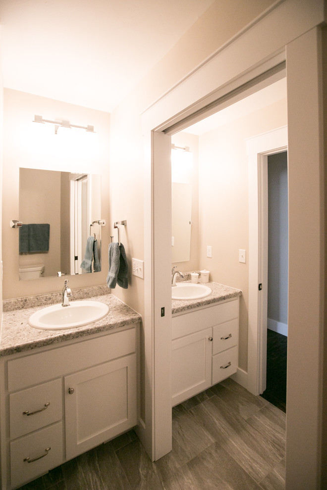 Exemple d'une salle de bain craftsman pour enfant avec un placard à porte plane, des portes de placard blanches, un carrelage gris, un mur gris, un sol en vinyl, un lavabo posé et un plan de toilette en stratifié.