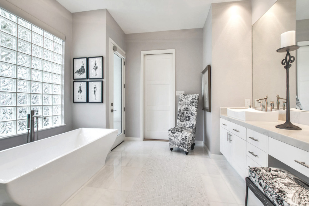 На фото: большая главная ванная комната в стиле модернизм с фасадами в стиле шейкер, белыми фасадами, отдельно стоящей ванной, душем без бортиков, белой плиткой, керамогранитной плиткой, серыми стенами, мраморным полом, настольной раковиной, мраморной столешницей, белым полом, душем с распашными дверями и белой столешницей