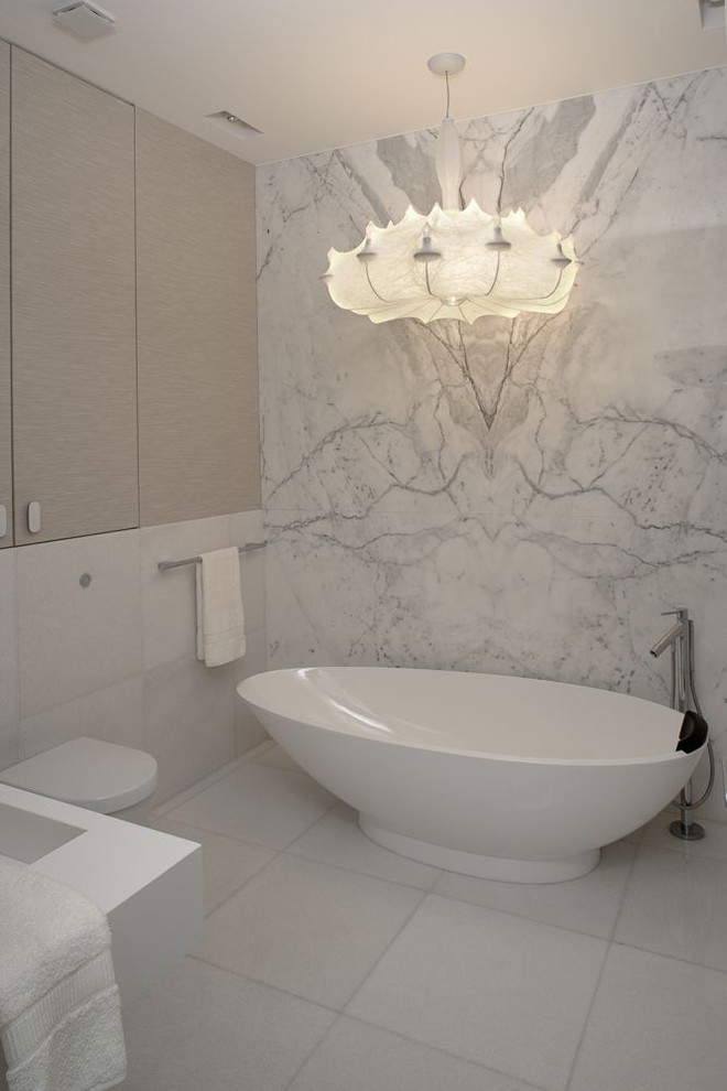 This is an example of a contemporary bathroom with a freestanding bath, a wall mounted toilet and marble tiles.