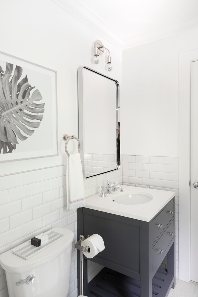Photo of a small rural family bathroom in Philadelphia with flat-panel cabinets, grey cabinets, an alcove bath, a shower/bath combination, a two-piece toilet, white tiles, ceramic tiles, white walls, porcelain flooring, a submerged sink and solid surface worktops.