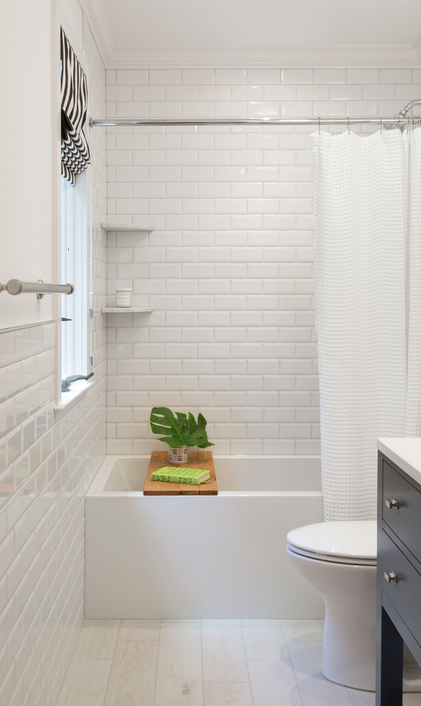 Foto på ett litet lantligt badrum med dusch, med släta luckor, grå skåp, ett badkar i en alkov, en dusch/badkar-kombination, en toalettstol med separat cisternkåpa, vit kakel, keramikplattor, vita väggar, klinkergolv i porslin, ett undermonterad handfat och bänkskiva i akrylsten
