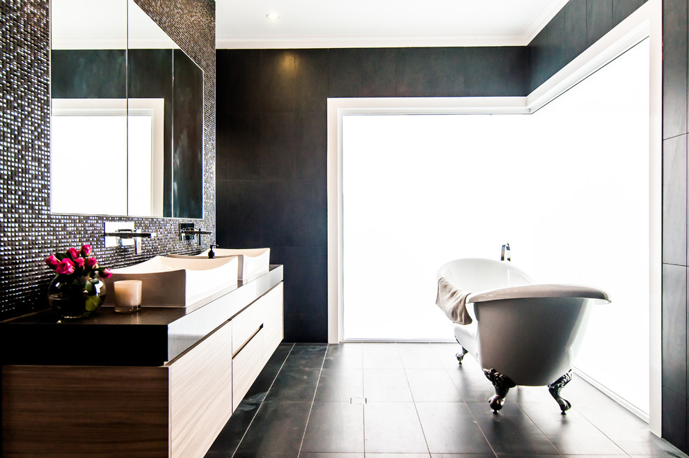 Modelo de cuarto de baño principal actual de tamaño medio con bañera con patas, baldosas y/o azulejos negros, suelo de baldosas de cerámica, lavabo sobreencimera y encimeras blancas
