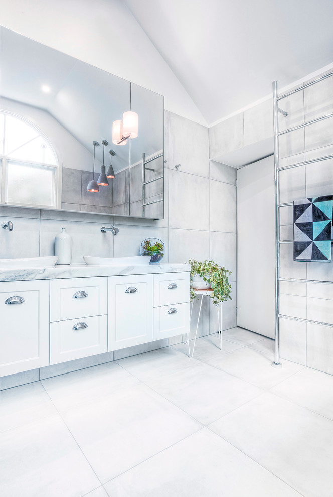 Cette photo montre une grande salle de bain principale tendance avec des portes de placard blanches, un plan de toilette en marbre, un carrelage gris, des carreaux de porcelaine, une vasque, un placard à porte shaker et un mur blanc.