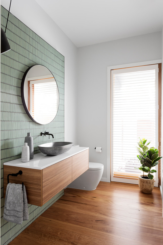 Modernes Badezimmer mit flächenbündigen Schrankfronten, hellbraunen Holzschränken, Wandtoilette mit Spülkasten, weißer Wandfarbe, braunem Holzboden, Aufsatzwaschbecken, braunem Boden und grauer Waschtischplatte in Melbourne