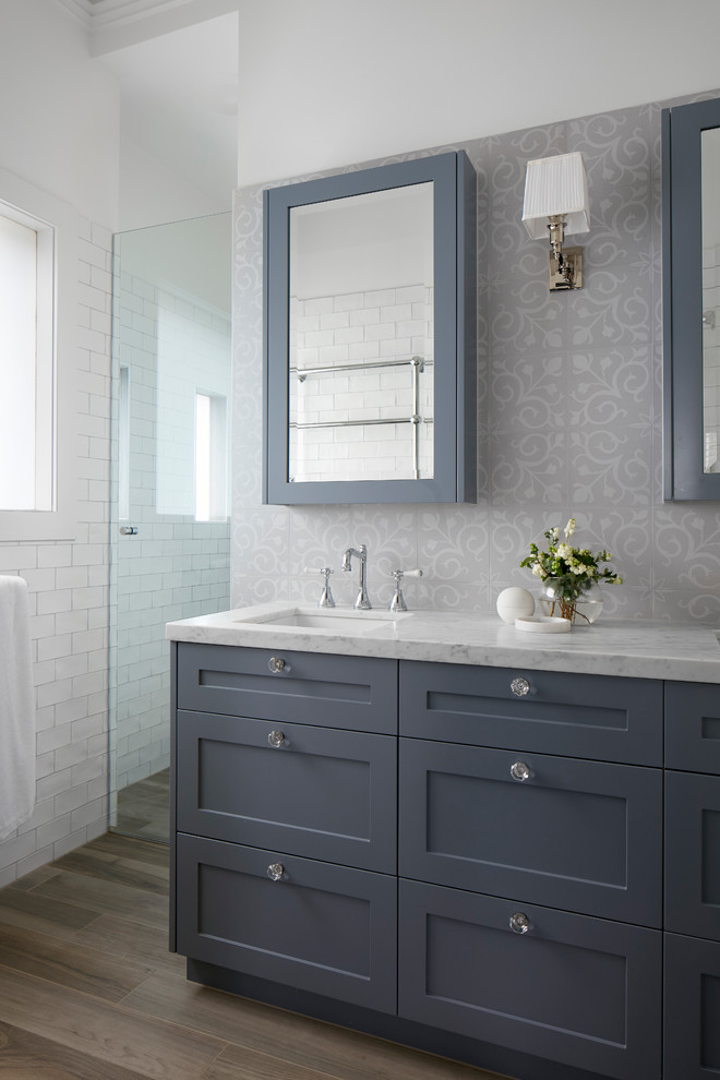 Klassisk inredning av ett mellanstort vit vitt badrum med dusch, med möbel-liknande, grå skåp, ett fristående badkar, en hörndusch, flerfärgad kakel, tunnelbanekakel, vita väggar, plywoodgolv, ett integrerad handfat, marmorbänkskiva, brunt golv och med dusch som är öppen