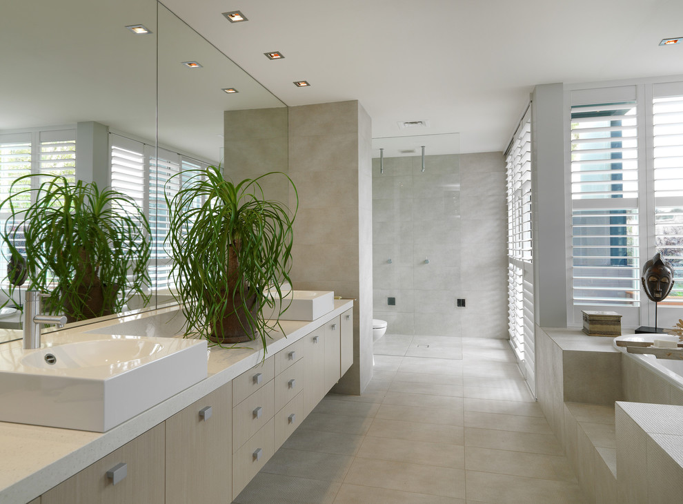 Inspiration for a large contemporary ensuite half tiled bathroom in Melbourne with a built-in shower, light wood cabinets, a built-in bath, a one-piece toilet, beige tiles, porcelain tiles, beige walls, porcelain flooring, a vessel sink, engineered stone worktops, beige floors, an open shower and flat-panel cabinets.