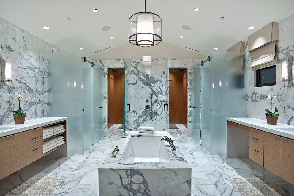 Пример оригинального дизайна: огромная главная ванная комната в современном стиле с плоскими фасадами, светлыми деревянными фасадами, отдельно стоящей ванной, двойным душем, белой плиткой, мраморной плиткой, белыми стенами, мраморным полом, врезной раковиной, мраморной столешницей, белым полом, душем с раздвижными дверями и белой столешницей