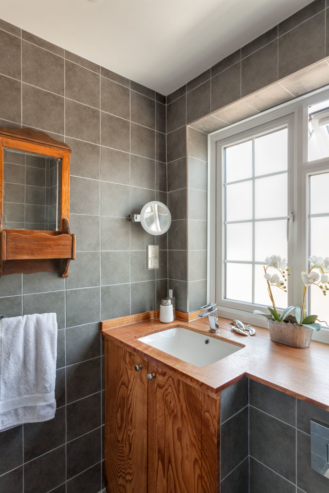 Contemporary bathroom in Sussex with flat-panel cabinets, medium wood cabinets, grey tiles, a submerged sink, wooden worktops and brown worktops.