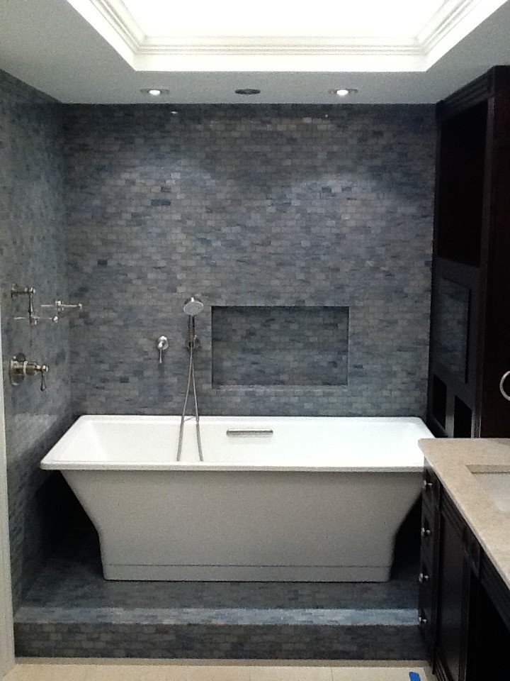 Foto di una stanza da bagno padronale contemporanea con lavabo integrato, ante a filo, ante in legno bruno, vasca freestanding, piastrelle blu, piastrelle in pietra, pareti multicolore e pavimento in marmo
