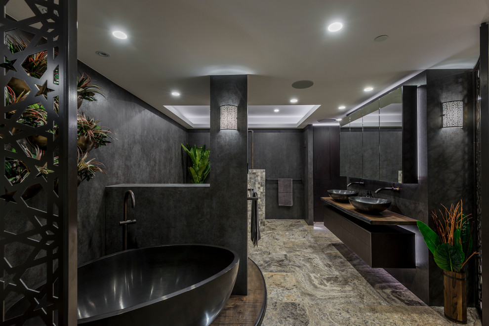 This is an example of a large contemporary ensuite bathroom in Brisbane with freestanding cabinets, dark wood cabinets, a freestanding bath, a corner shower, a wall mounted toilet, grey tiles, porcelain tiles, grey walls, travertine flooring, a vessel sink, wooden worktops, beige floors, an open shower and brown worktops.