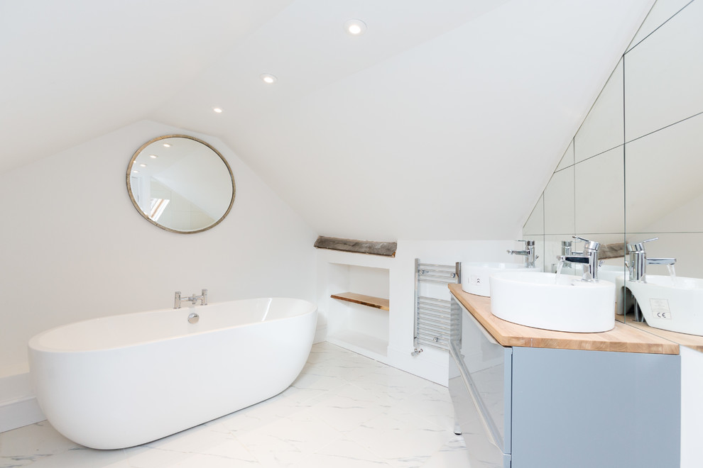 Contemporary ensuite bathroom in London with flat-panel cabinets, grey cabinets, a freestanding bath, white walls, a vessel sink, wooden worktops, white floors and brown worktops.