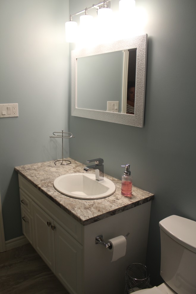 Photo of a medium sized traditional family bathroom in Toronto with shaker cabinets, white cabinets, an alcove bath, a shower/bath combination, a two-piece toilet, white tiles, ceramic tiles, blue walls, porcelain flooring, a built-in sink and laminate worktops.