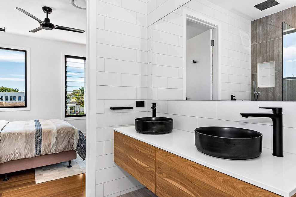 Cette image montre une grande salle de bain principale design en bois brun avec un placard à porte plane, une baignoire indépendante, un carrelage blanc, des carreaux de porcelaine, un mur blanc, un sol en carrelage de porcelaine et un sol gris.